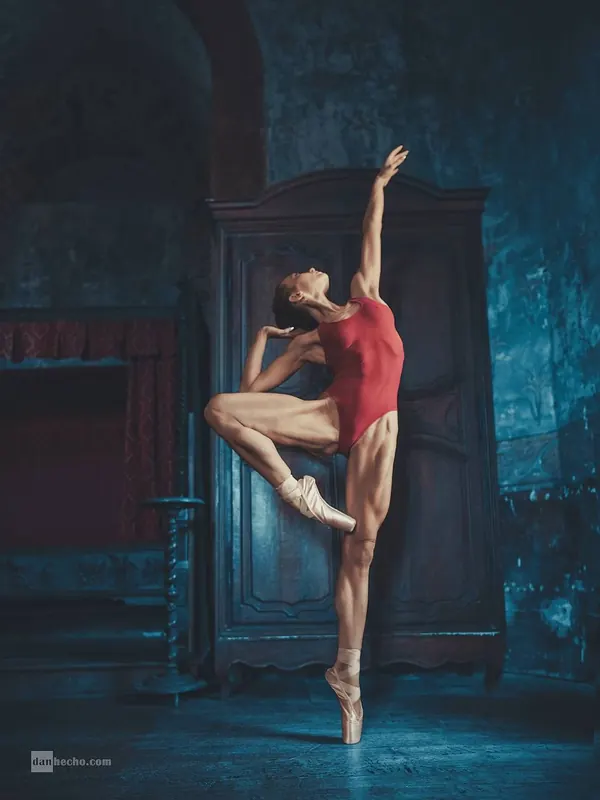 Zuza on pointe in a red leotard in a deep blue doorway
