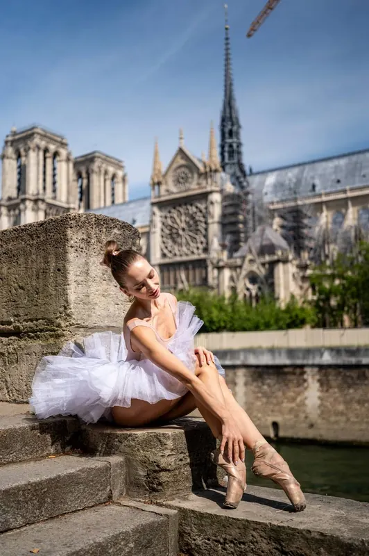 Zuza resting on stone steps in a tutu, Notre-Dame behind her