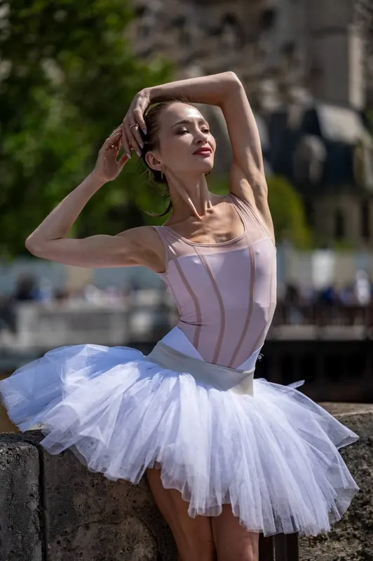 Zuza smiling in a white tutu by the Seine, arms raised