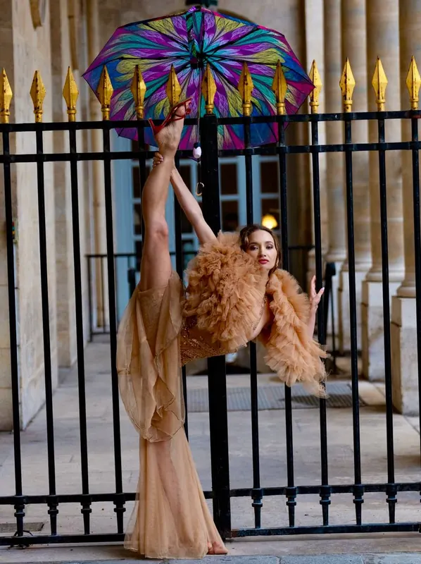 Zuza at a gilded gate with a rainbow umbrella